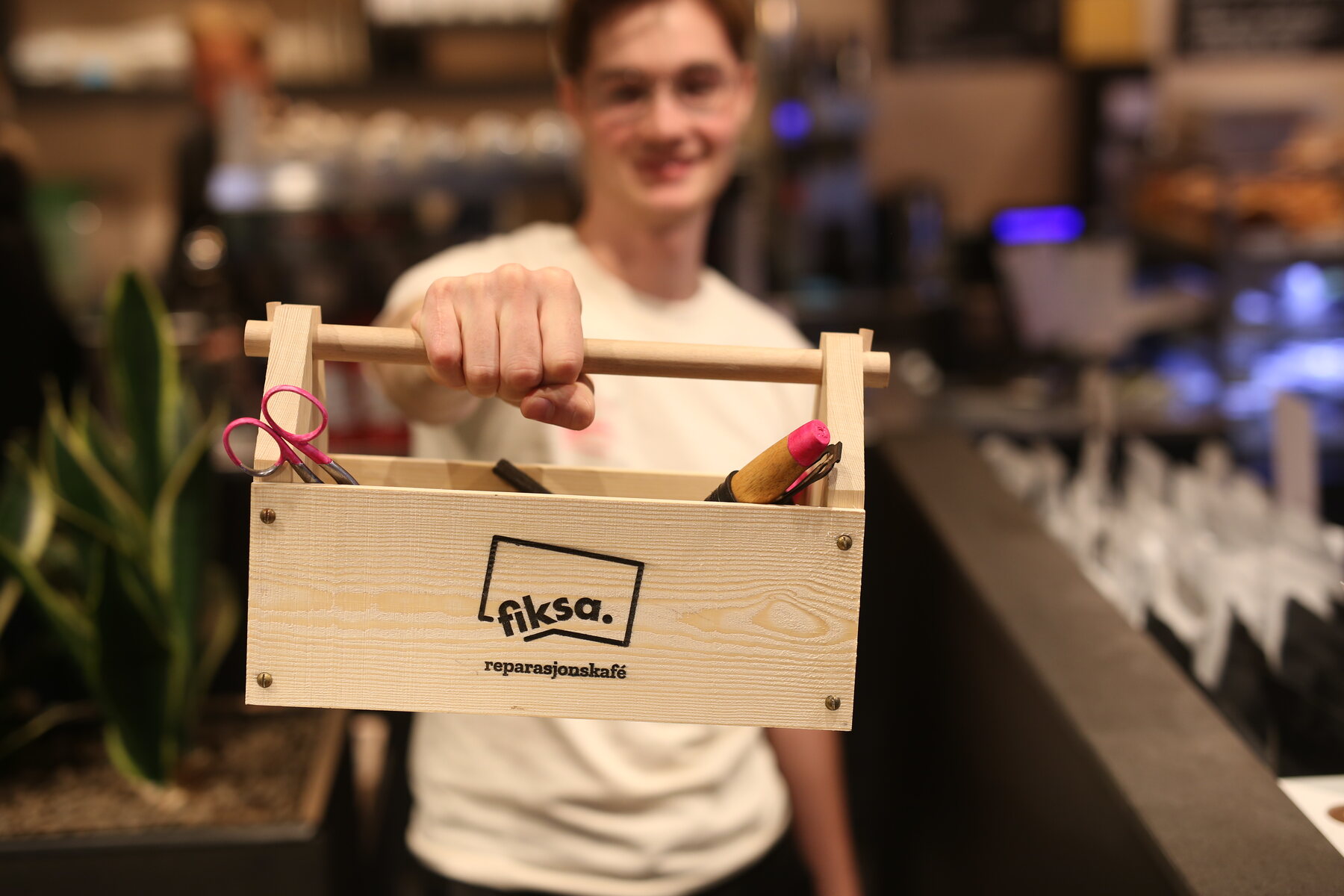 A hand holding the wooden Fiksa toolbox with scissors and a pencil inside