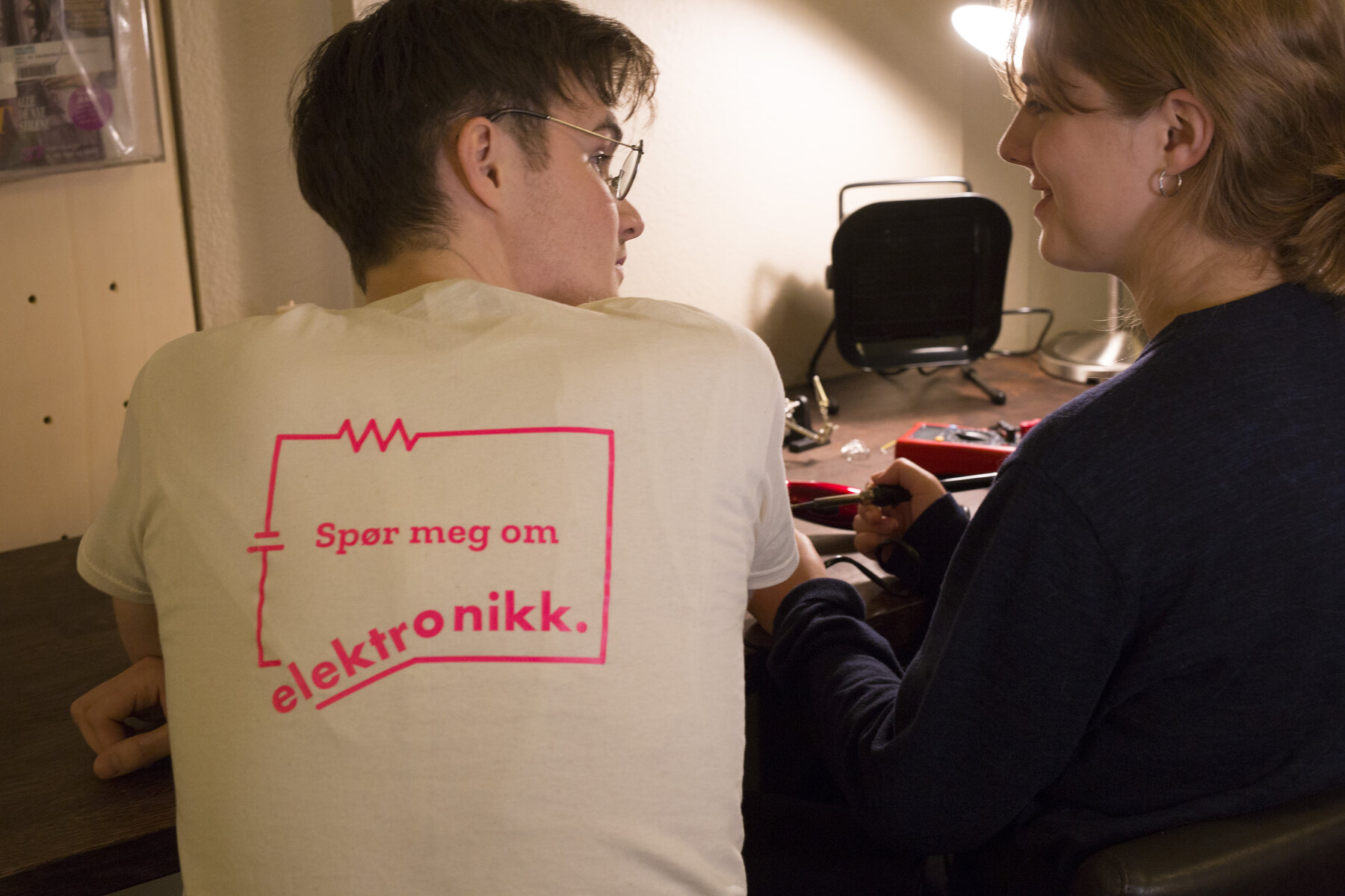 Back of a t-shirt printed “Spør meg om elektronikk”