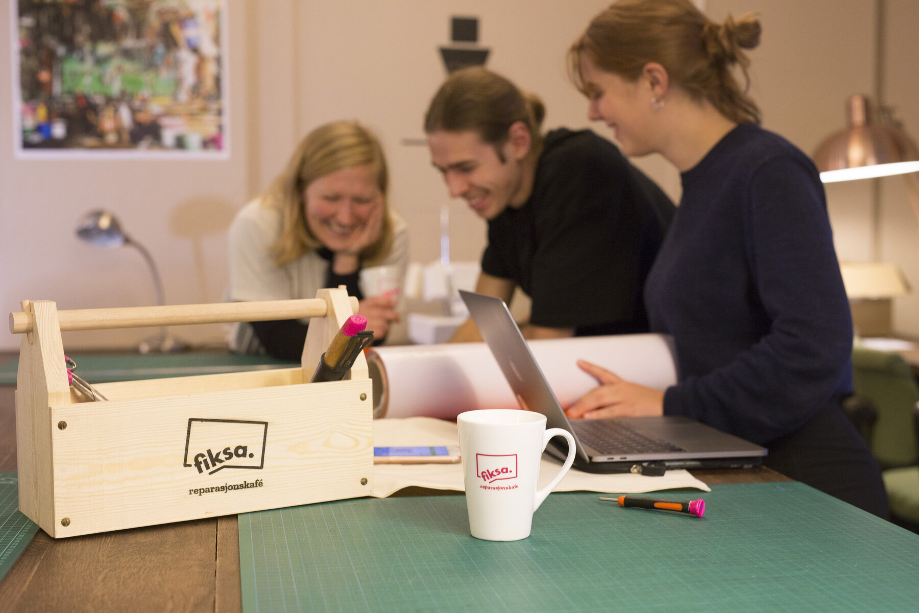 Three people at a table with laptop, Fiksa toolbox and mug